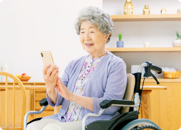 車椅子に座りながらスマートフォンを操作している笑顔の高齢女性